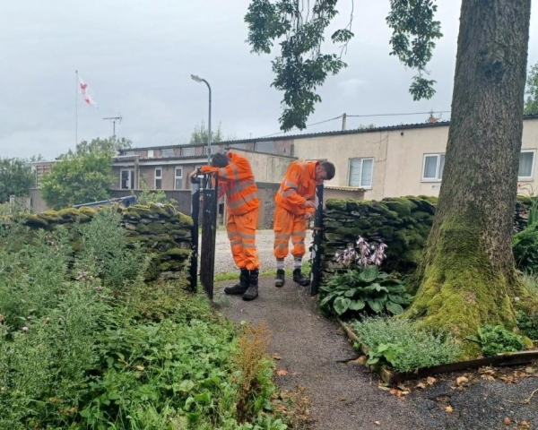 Two men in orange high vis paining an iron fence in a church yard