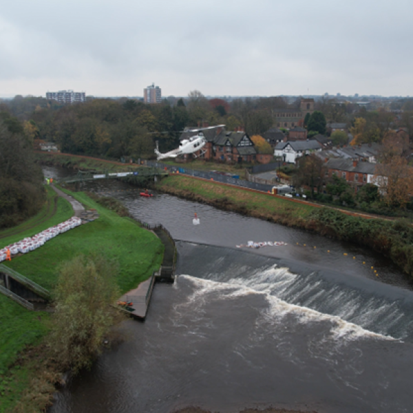 Picture of a helicopter carrying a bulk bag over a river.