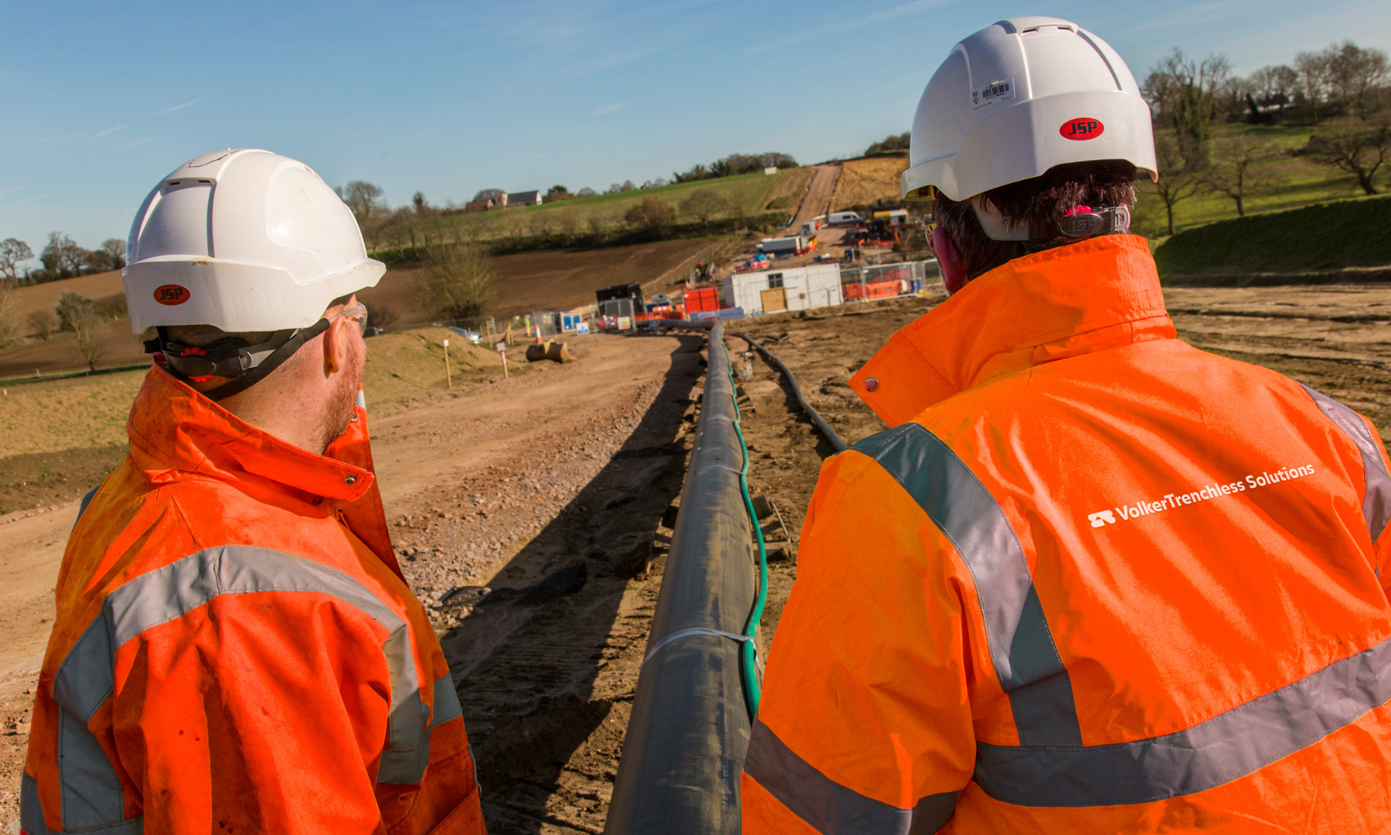 Two men in orange PPE looking down a pipeline route